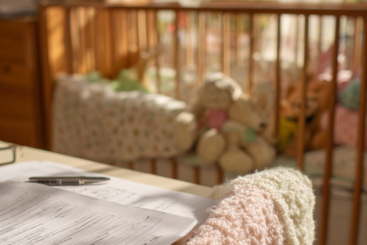 Habitación infantil por la noche: una cuna, una mantita de bebé sobre el respaldo de una silla, notas y un bolígrafo al lado.