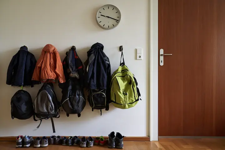 Giacche, zaini e scarpe di bambini all’ingresso di un appartamento di famiglia, sopra un orologio a muro